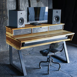 A rustic, industrial-style computer desk made from reclaimed wood and scrap metal, styled with a computer monitor, two speakers, and a black office chair in a dark, moody room.