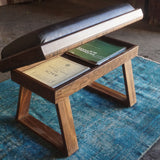 A wooden bench with a black cushioned top and open storage compartment, placed on a blue rug in a rustic workshop setting.
