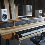 Wooden studio desk with electronic keyboard, computer monitor, and speakers in a rustic room.
