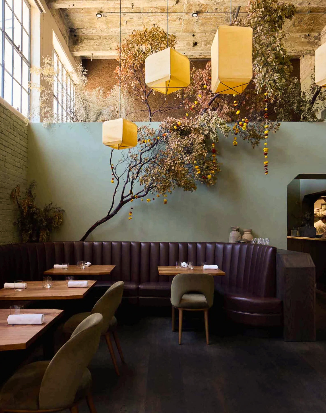 A dark, atmospheric interior hallway looking into a dining or bar area with a long wooden table, chairs, and two hanging warm-white pendant lights.