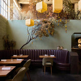 A dark, atmospheric interior hallway looking into a dining or bar area with a long wooden table, chairs, and two hanging warm-white pendant lights.